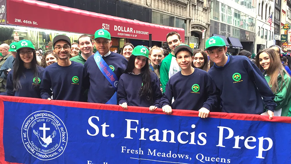 Students and staff from St. Francis Preparatory School holding a school banner during a St. Patrick’s Day parade on a city street.
